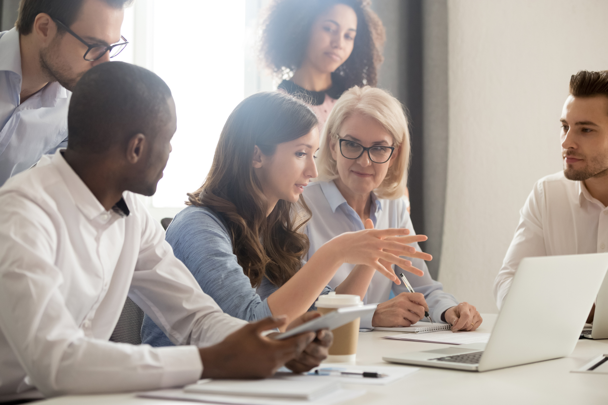 Young female mentor leader coach teaching employees group analyzing online project explaining business strategy speaking training diverse corporate team with laptop using computer at office meeting